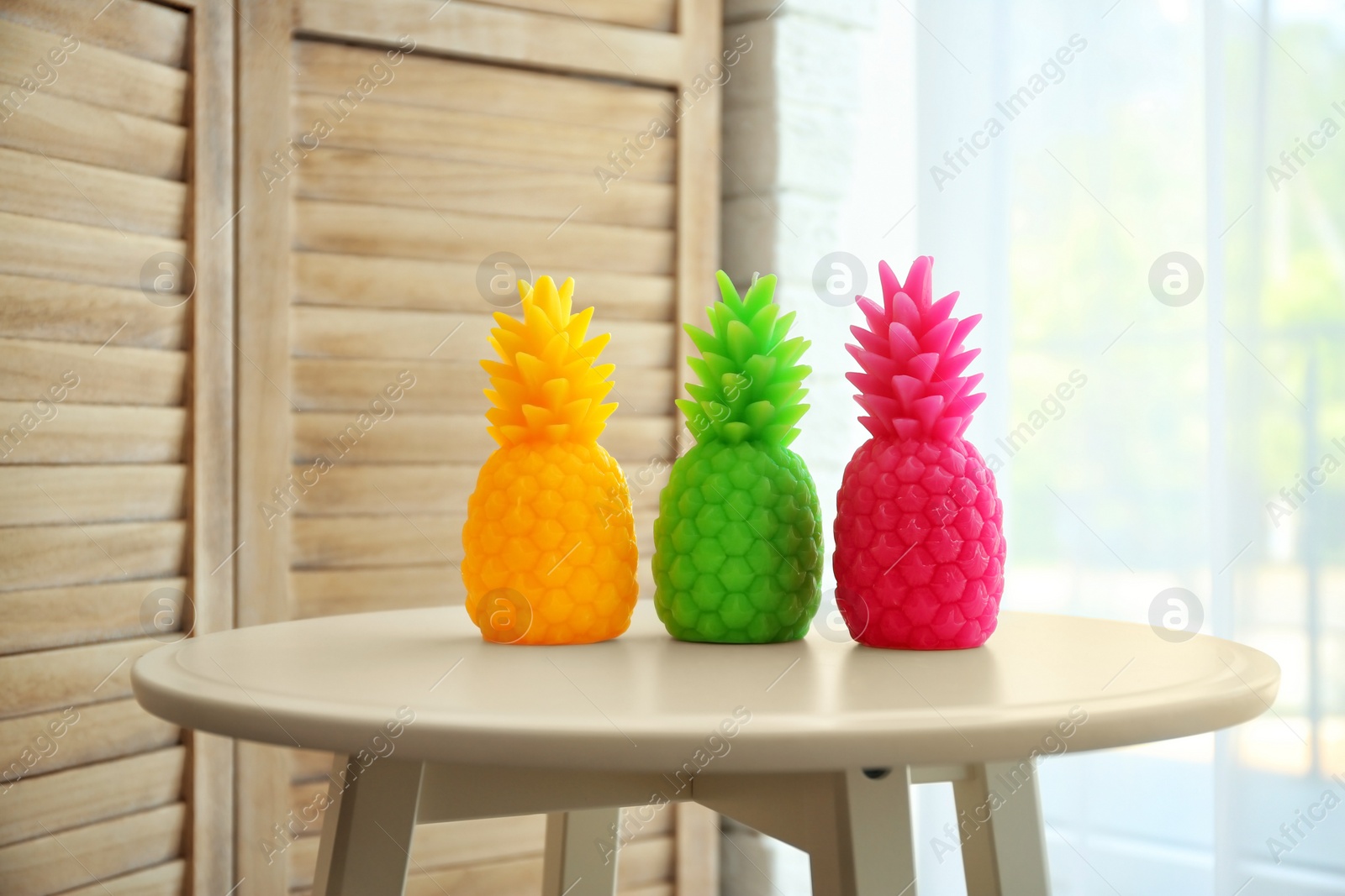 Photo of Stylish pineapple candles on table indoors. Home decorating idea