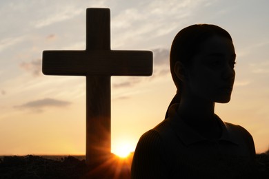 Image of Atheism. Silhouette of woman turned away from Christian cross outdoors at sunrise