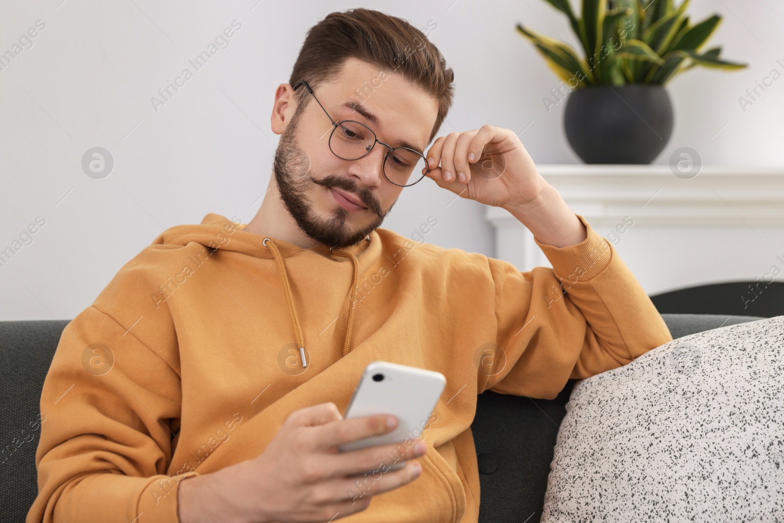 Photo of Man using smartphone on grey sofa in cozy room