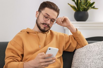 Man using smartphone on grey sofa in cozy room