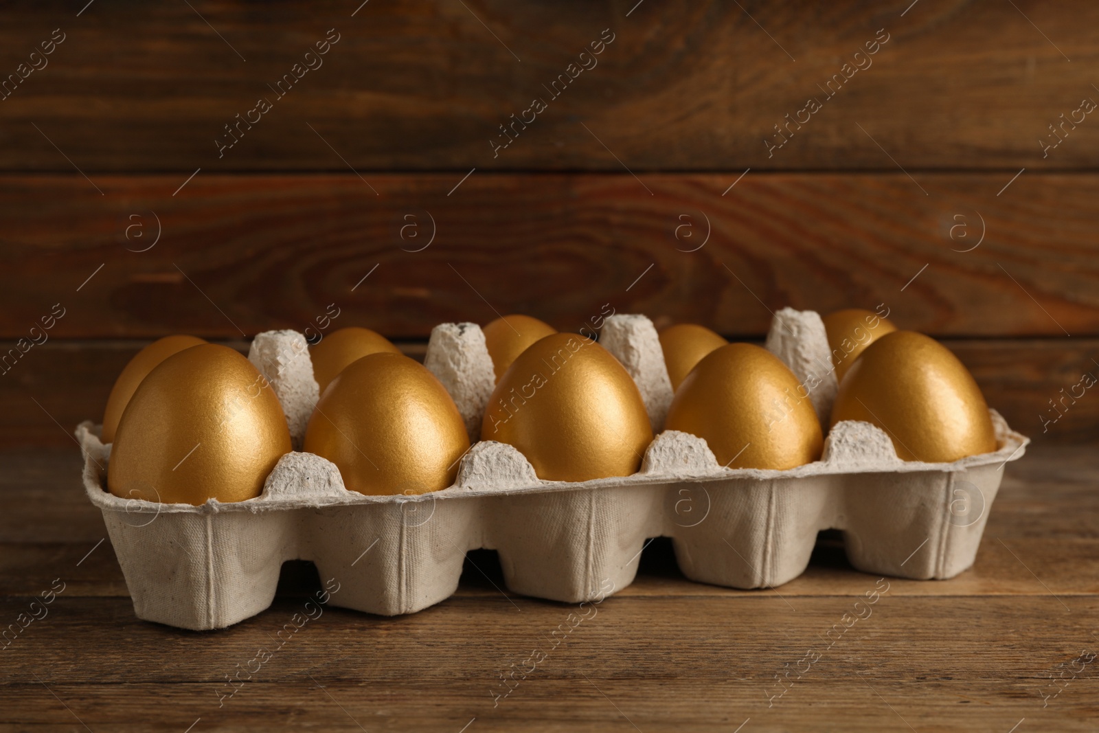 Photo of Carton with golden eggs on wooden table