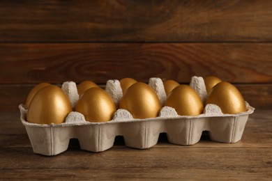 Carton with golden eggs on wooden table