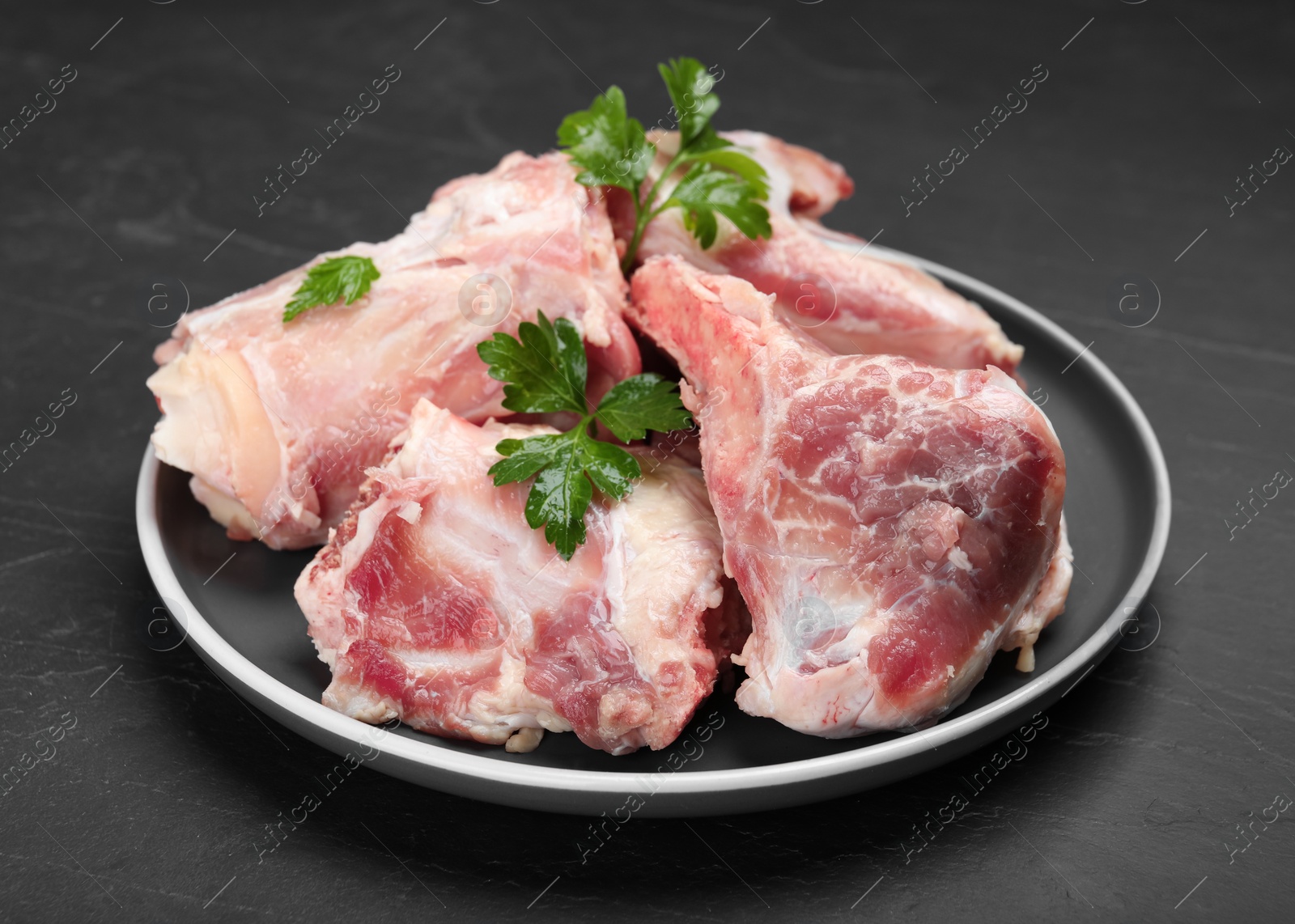 Photo of Plate with raw chopped meaty bones and parsley on black table