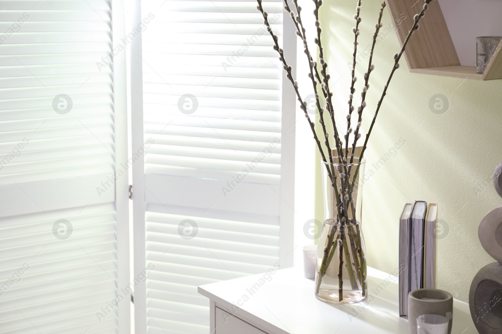 Photo of Glass vase with pussy willow tree branches and decor on white table in room