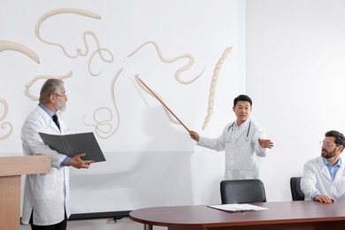 Professors giving lecture in gastroenterology. Projection screen with illustration of helminths