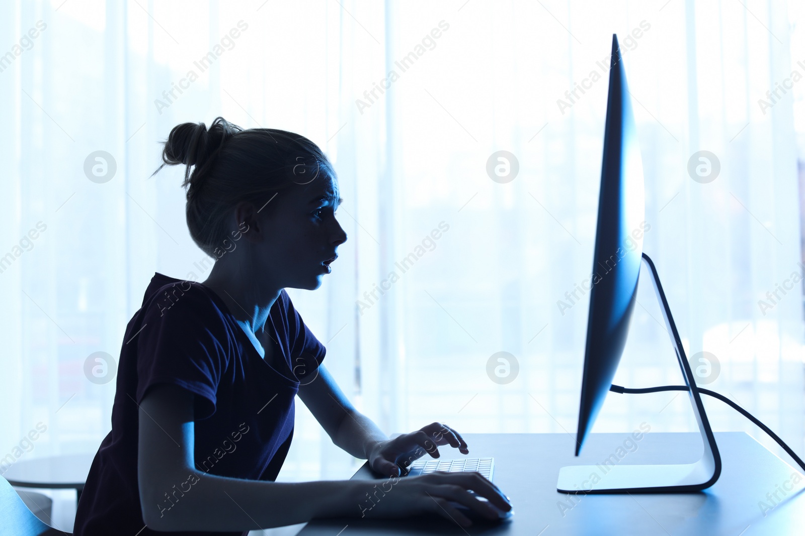 Photo of Shocked teenage girl using computer at table indoors. Danger of internet