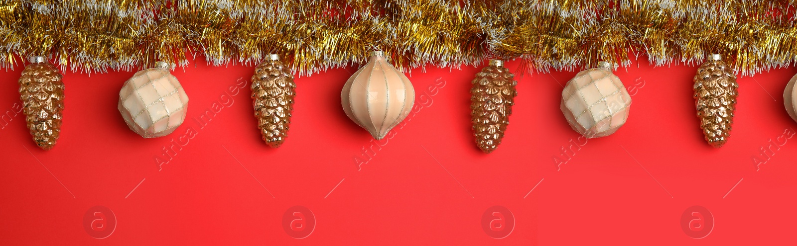Image of Shiny golden tinsel and Christmas baubles on red background, flat lay. Banner design