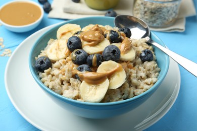 Photo of Tasty oatmeal with banana, blueberries and peanut butter served in bowl on light blue wooden table