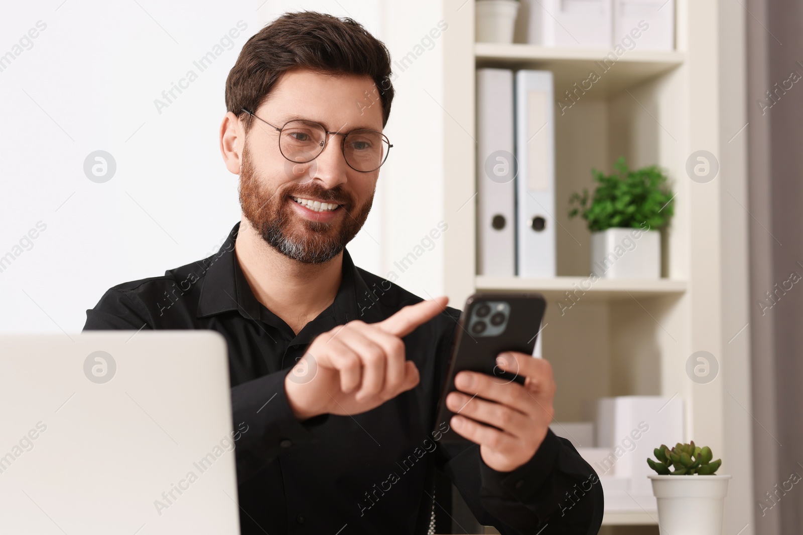 Photo of Smiling man in shirt using smartphone in office