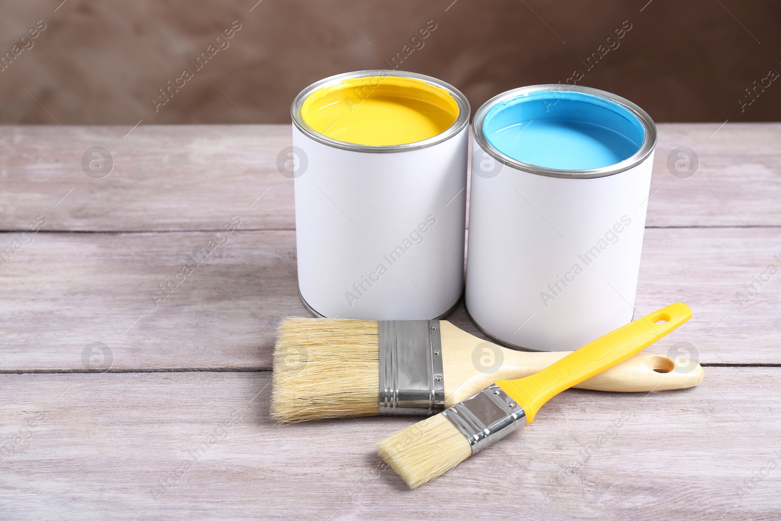 Photo of Cans of colorful paints with brushes on wooden table
