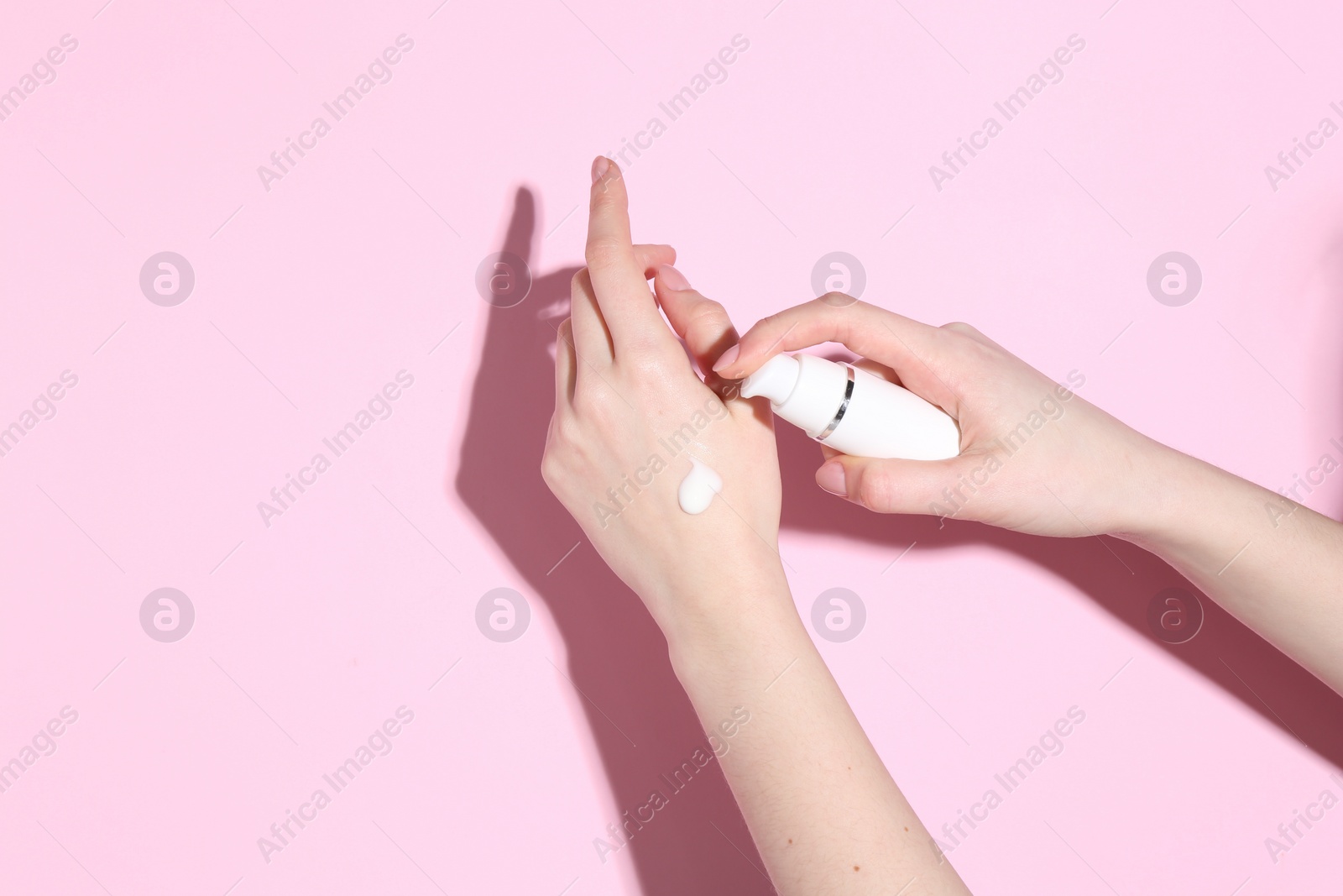 Photo of Woman applying cream on her hand against pink background, closeup