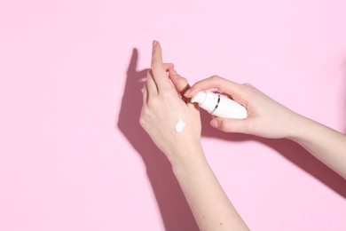 Photo of Woman applying cream on her hand against pink background, closeup