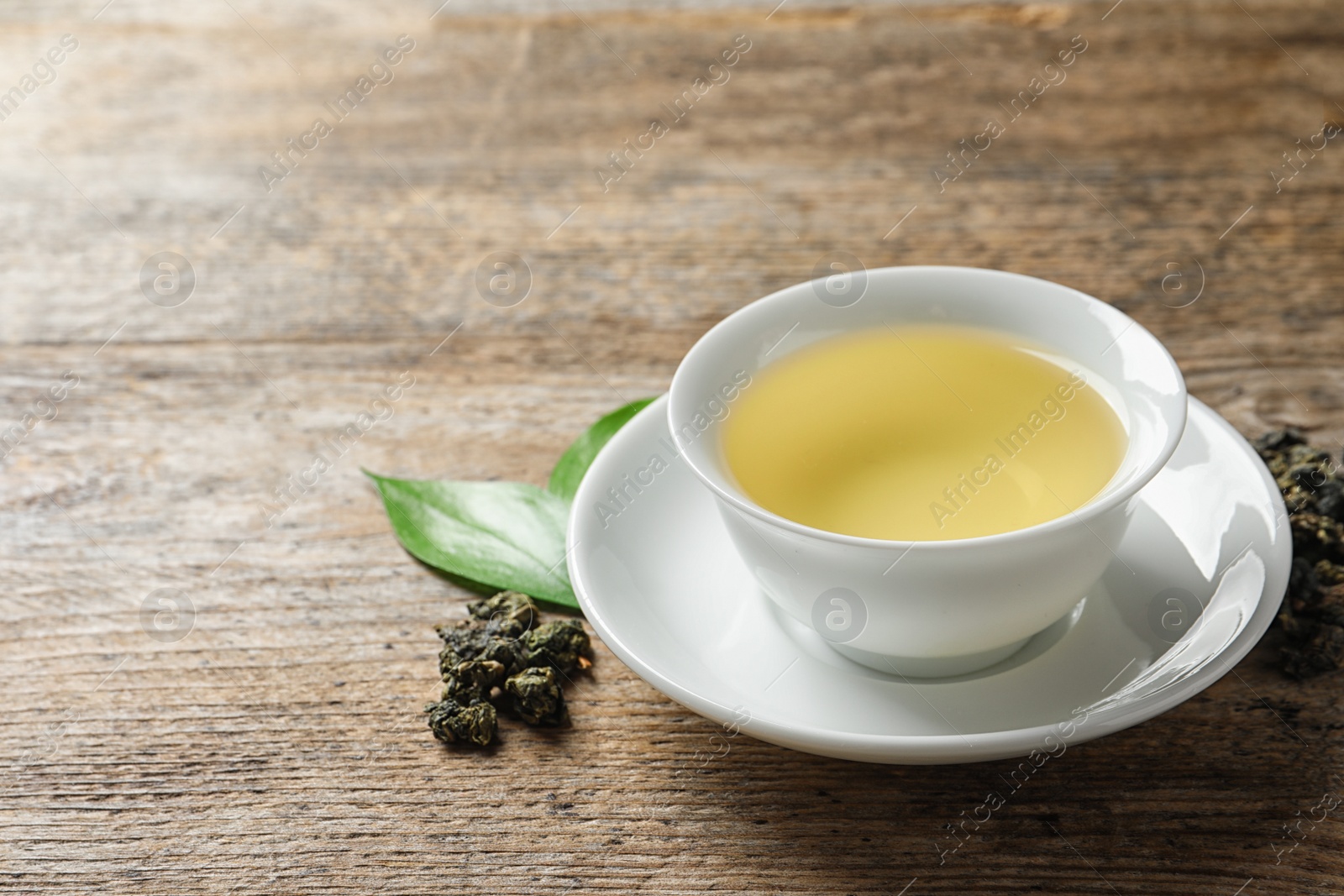 Photo of Cup of Tie Guan Yin oolong and tea leaves on wooden table. Space for text