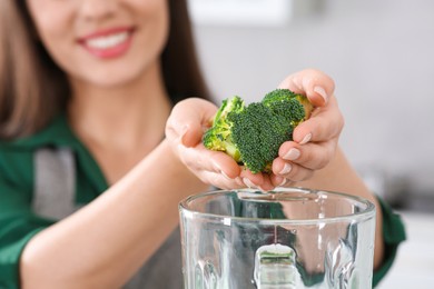 Photo of Woman adding broccoli into blender for smoothie on blurred background, closeup