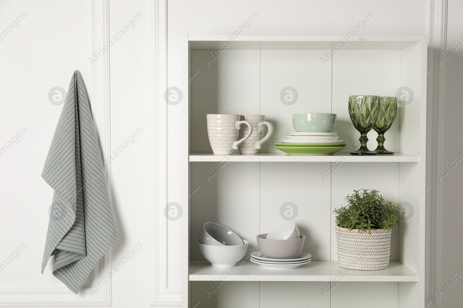 Photo of Different clean dishware and houseplant on shelves in cabinet indoors