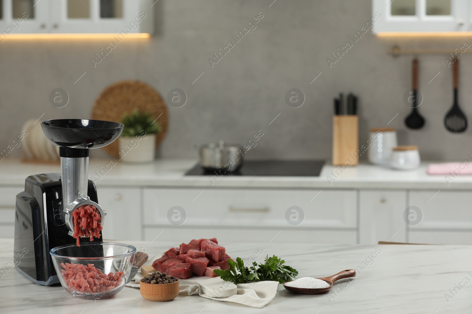 Photo of Electric meat grinder with beef mince, parsley, salt and peppercorns on white table in kitchen