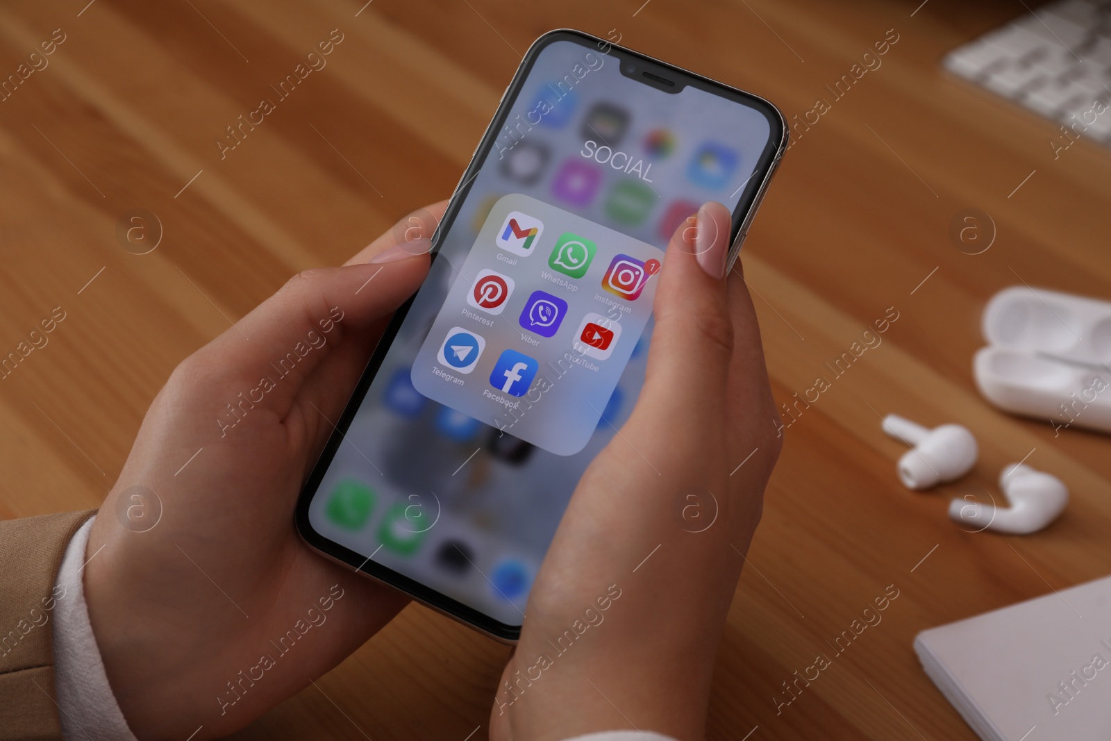 Photo of MYKOLAIV, UKRAINE - AUGUST 11, 2021: Woman using Apple iPhone X at wooden table, closeup. Screen with different social media icons