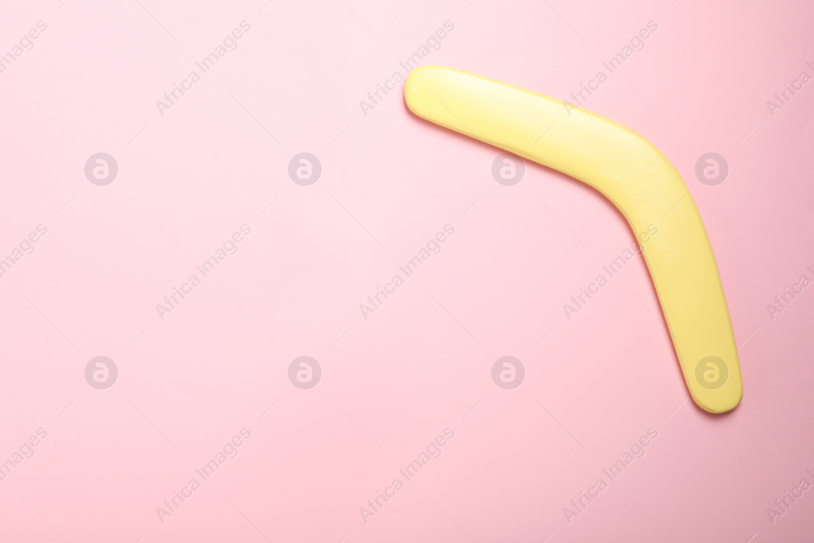 Photo of Yellow wooden boomerang on pink background, top view. Space for text