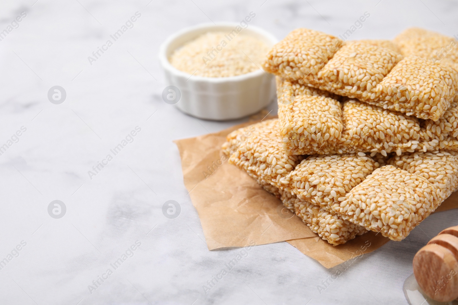 Photo of Delicious sweet kozinaki bars, sesame seeds and wooden dipper on white marble table, closeup. Space for text