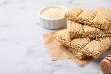 Delicious sweet kozinaki bars, sesame seeds and wooden dipper on white marble table, closeup. Space for text