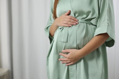 Photo of Pregnant woman in green dressing gown near window indoors, closeup. Space for text