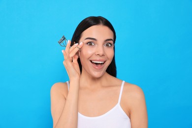 Photo of Emotional young woman with eyelash curler on light blue background