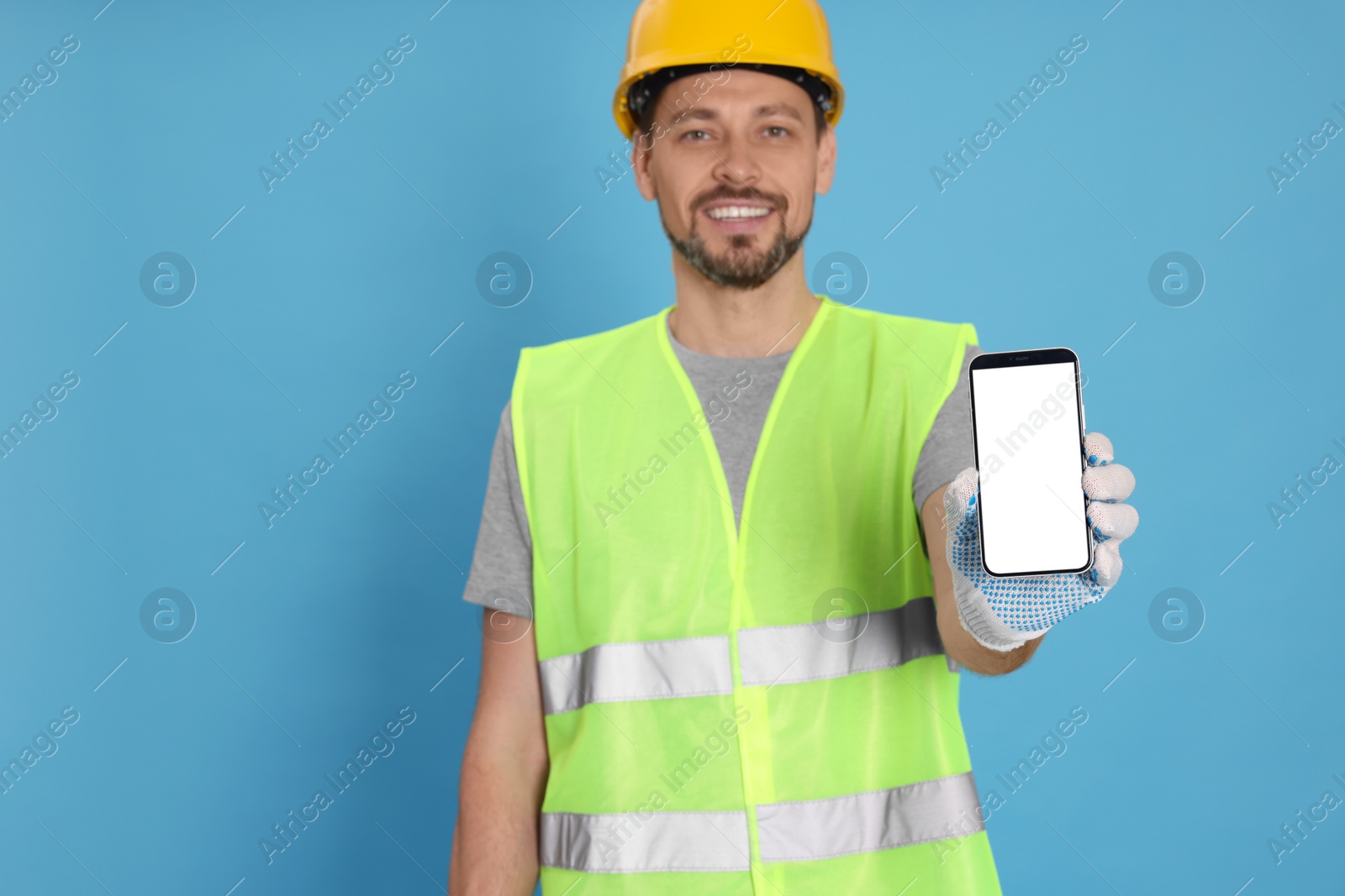 Photo of Male industrial engineer in uniform with phone on light blue background