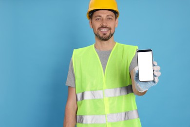 Photo of Male industrial engineer in uniform with phone on light blue background