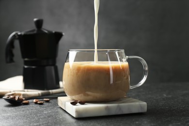 Photo of Pouring milk into glass cup with coffee at dark textured table, closeup