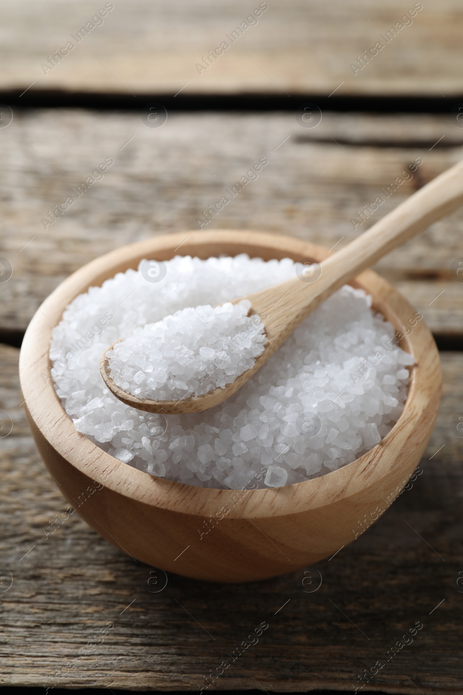 Photo of Organic salt in bowl and spoon on wooden table, closeup