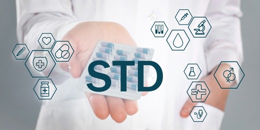 Image of STD prevention. Closeup view of doctor with pills, abbreviation and different icons on light background, banner design