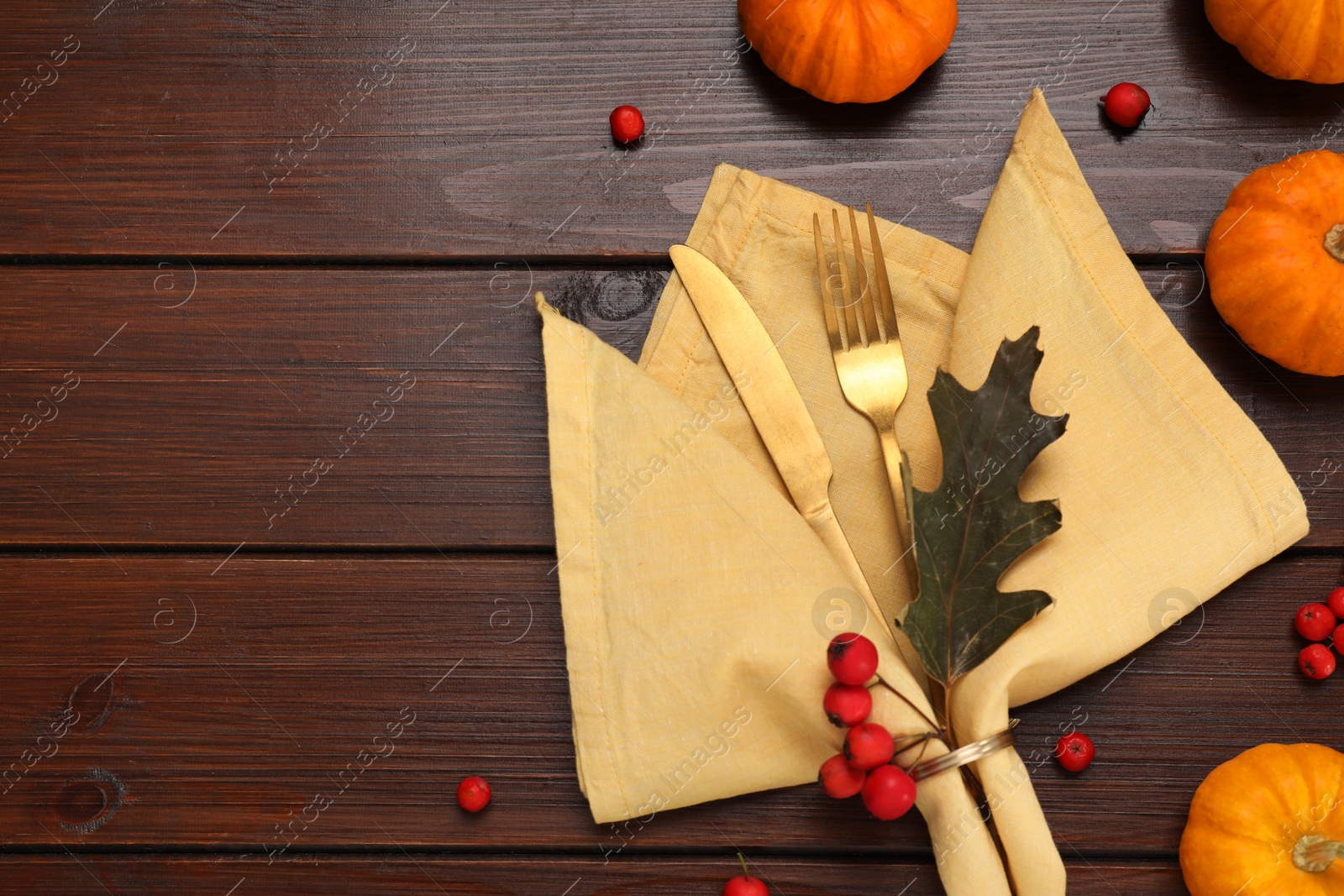 Photo of Cutlery, napkin and autumn decoration on wooden background, flat lay with space for text. Table setting