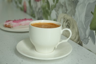 Photo of Cup of delicious aromatic coffee and eclair on white table indoors, closeup