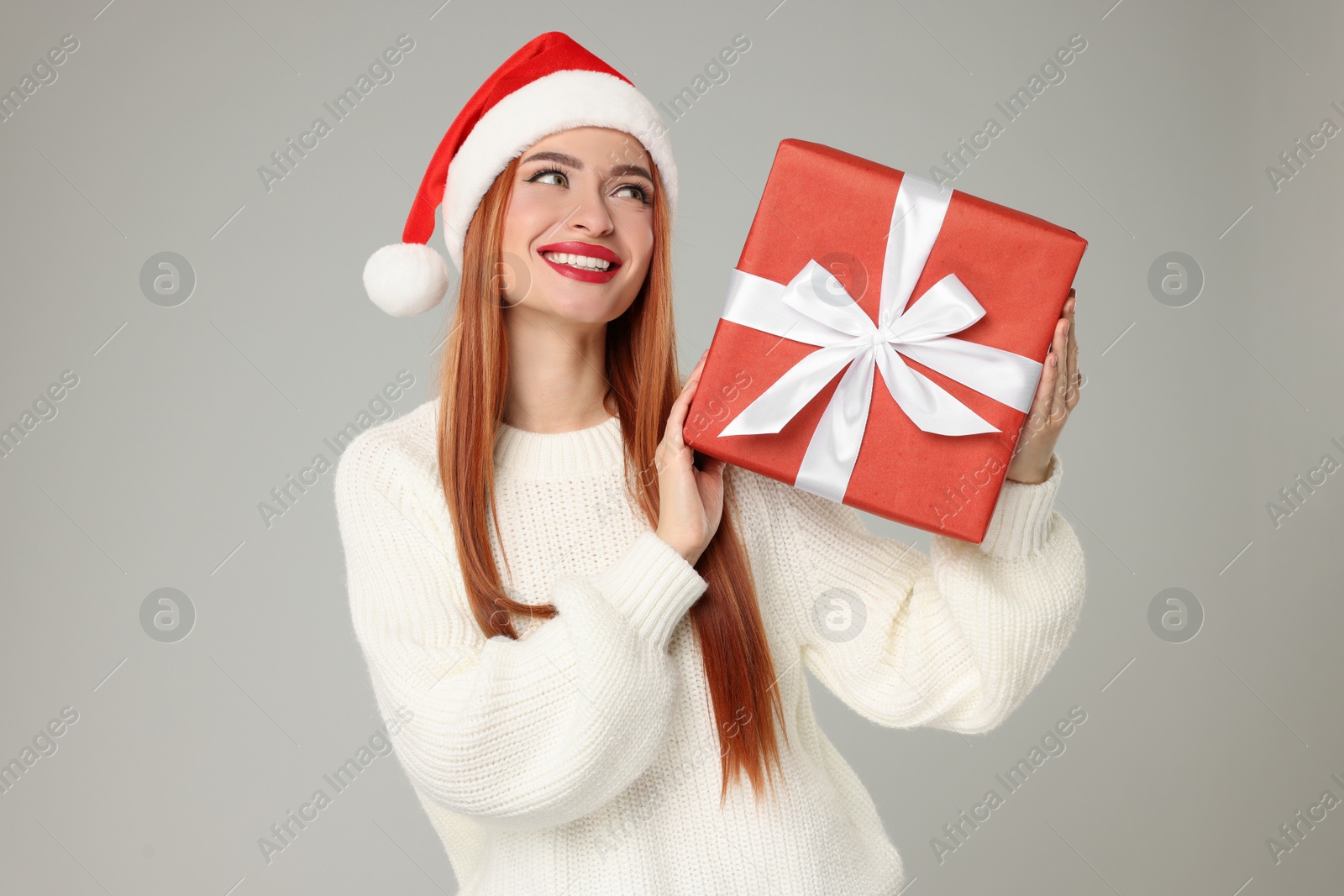 Photo of Young woman in Santa hat with Christmas gift on light grey background