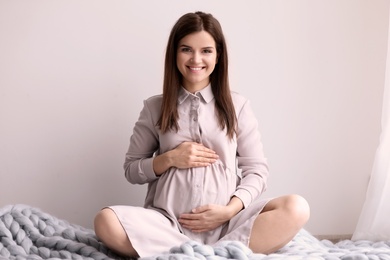 Young pregnant woman sitting on warm blanket indoors