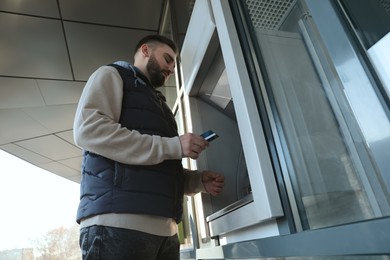 Photo of Man with credit card near cash machine outdoors, low angle view
