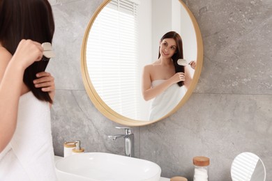 Beautiful woman brushing her hair near mirror in bathroom