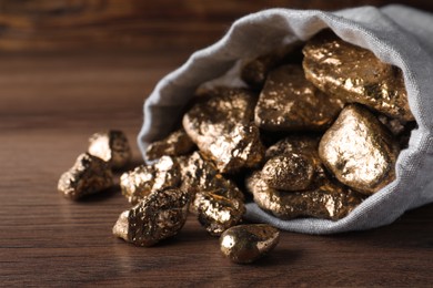 Photo of Overturned sack of gold nuggets on wooden table, closeup