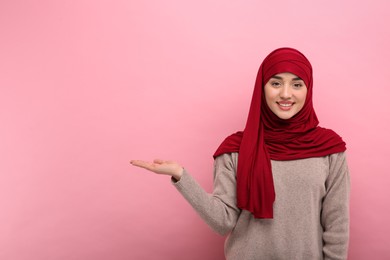 Photo of Muslim woman in hijab pointing at something on pink background, space for text