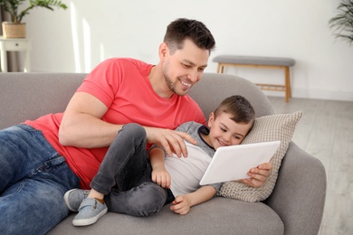 Photo of Boy and his father with tablet lying on sofa at home. Family time