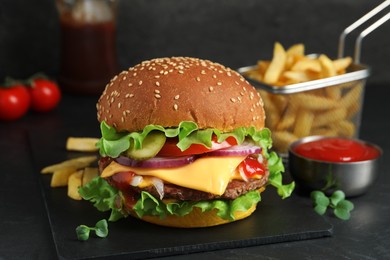 Photo of Delicious burger with beef patty, french fries and tomato sauce on dark table