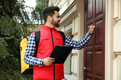 Photo of Courier with thermo bag and clipboard knocking on customer's house. Food delivery service