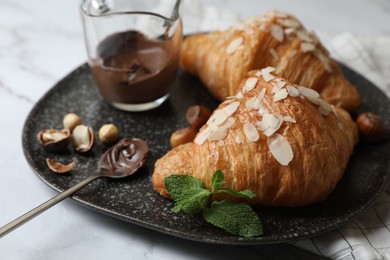 Photo of Delicious croissants with chocolate, nuts and spoon on white marble table, closeup