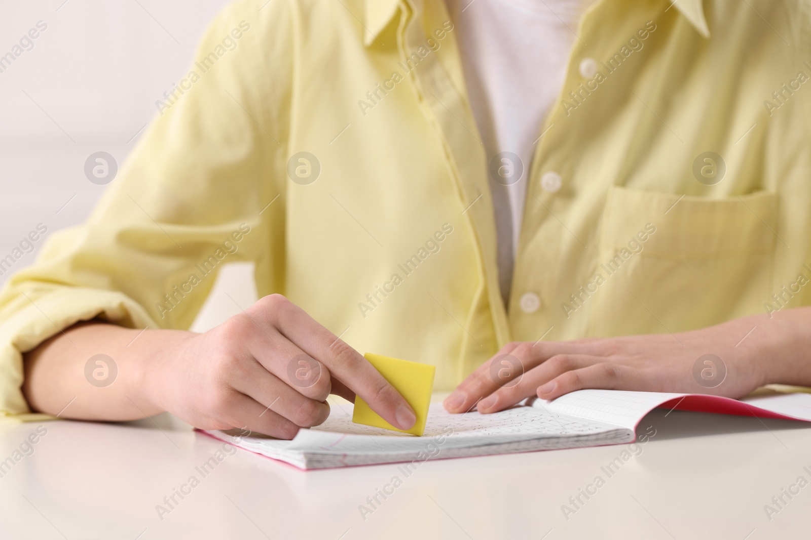 Photo of Girl erasing mistake in her notebook at white desk, closeup