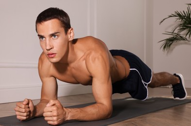 Photo of Handsome man doing plank exercise on floor indoors