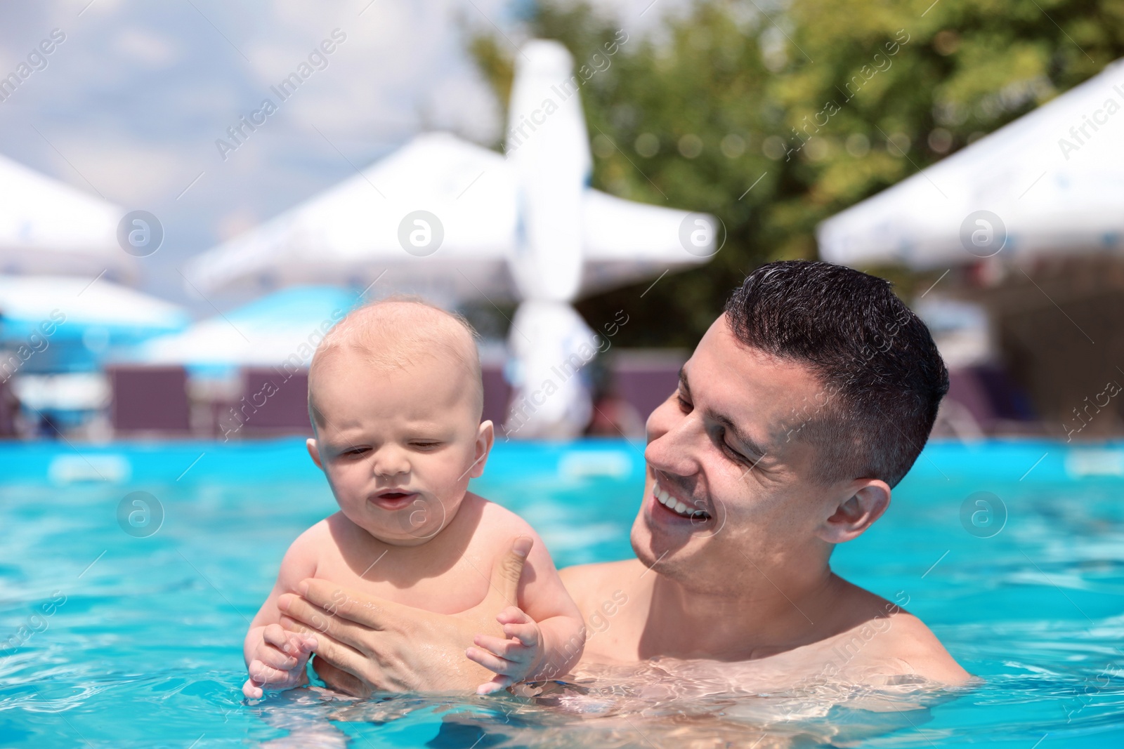 Photo of Man with his little baby in swimming pool on sunny day, outdoors