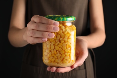 Woman holding jar with pickled corn against black background, closeup