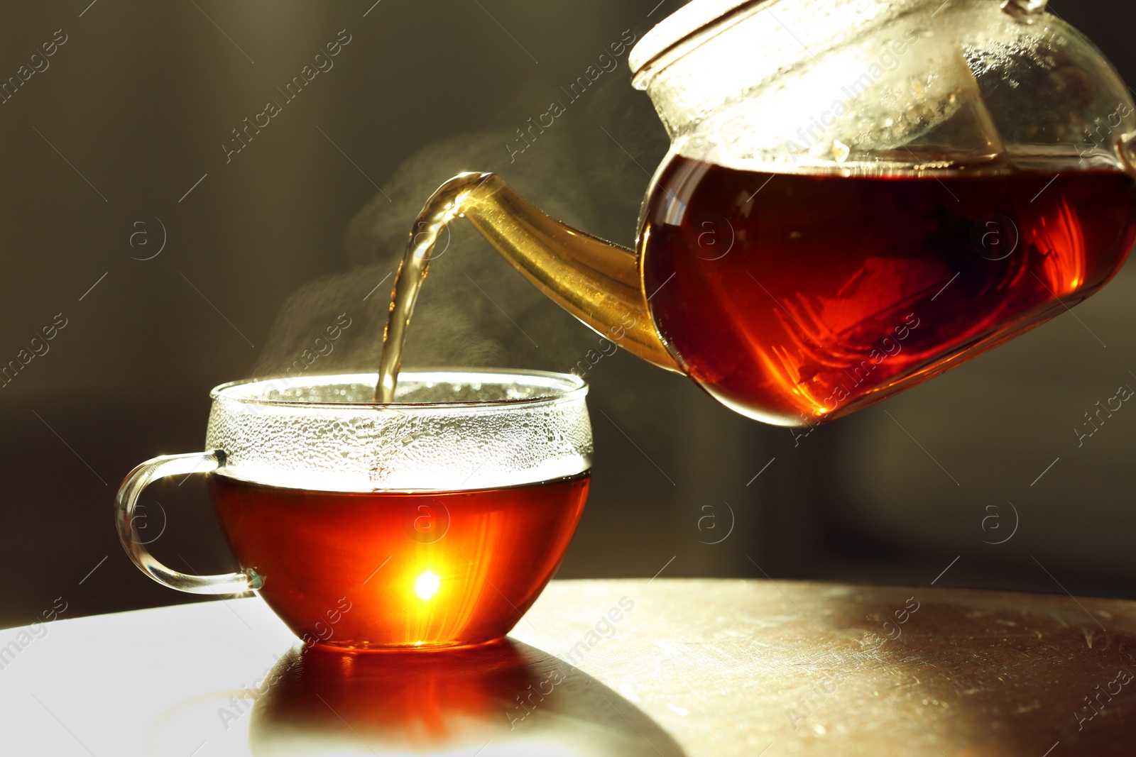 Photo of Pouring fresh hot tea from teapot into cup against blurred background, closeup