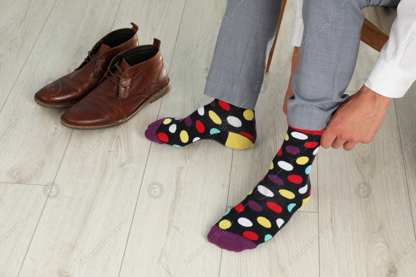 Photo of Man putting on colorful socks indoors, closeup