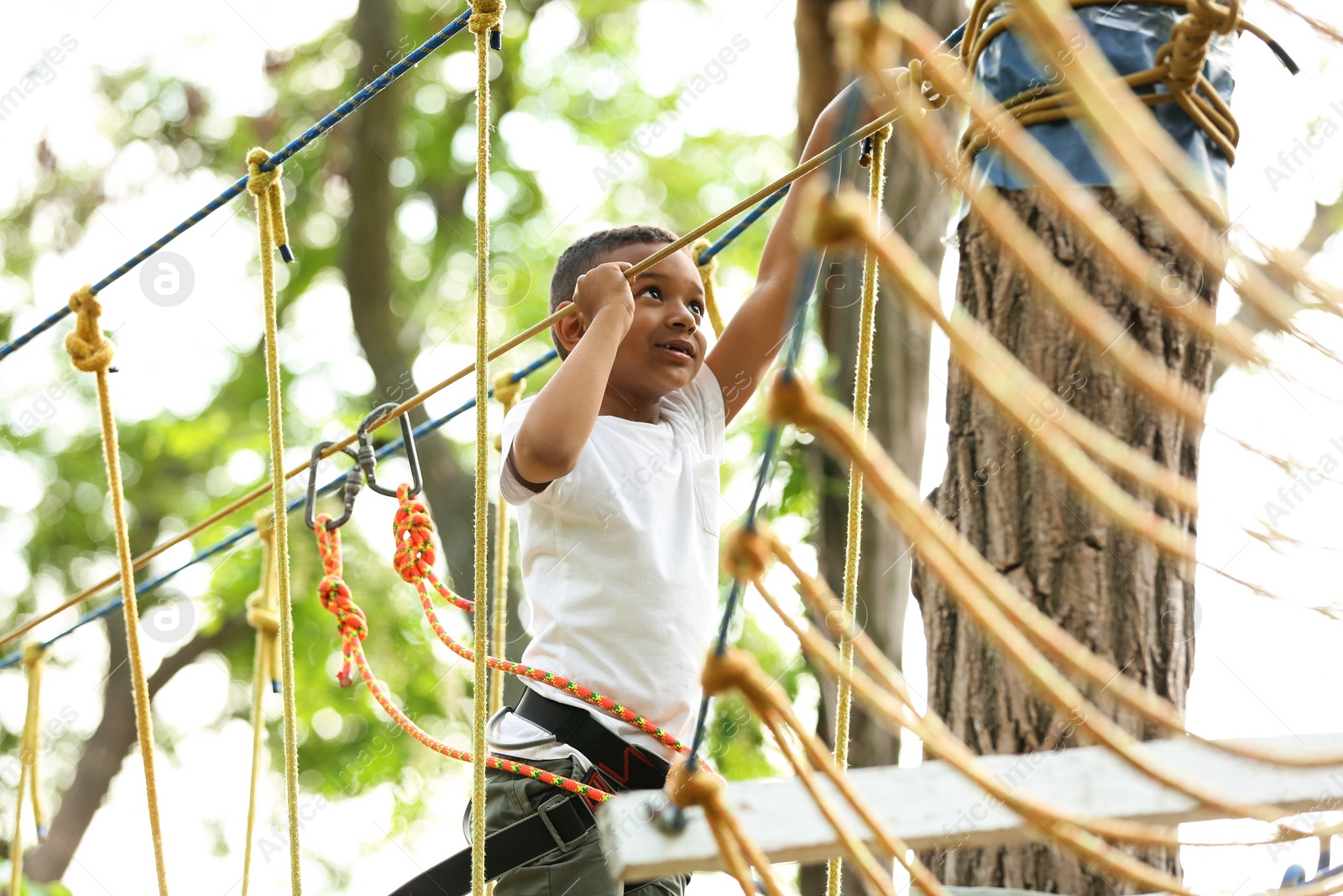 Photo of Little African-American boy climbing in adventure park. Summer camp